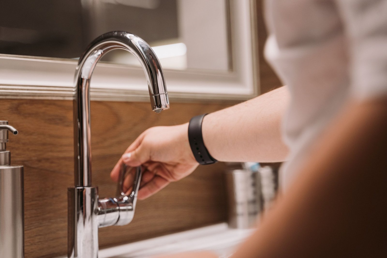 Person turning on a modern chrome kitchen faucet in a contemporary kitchen