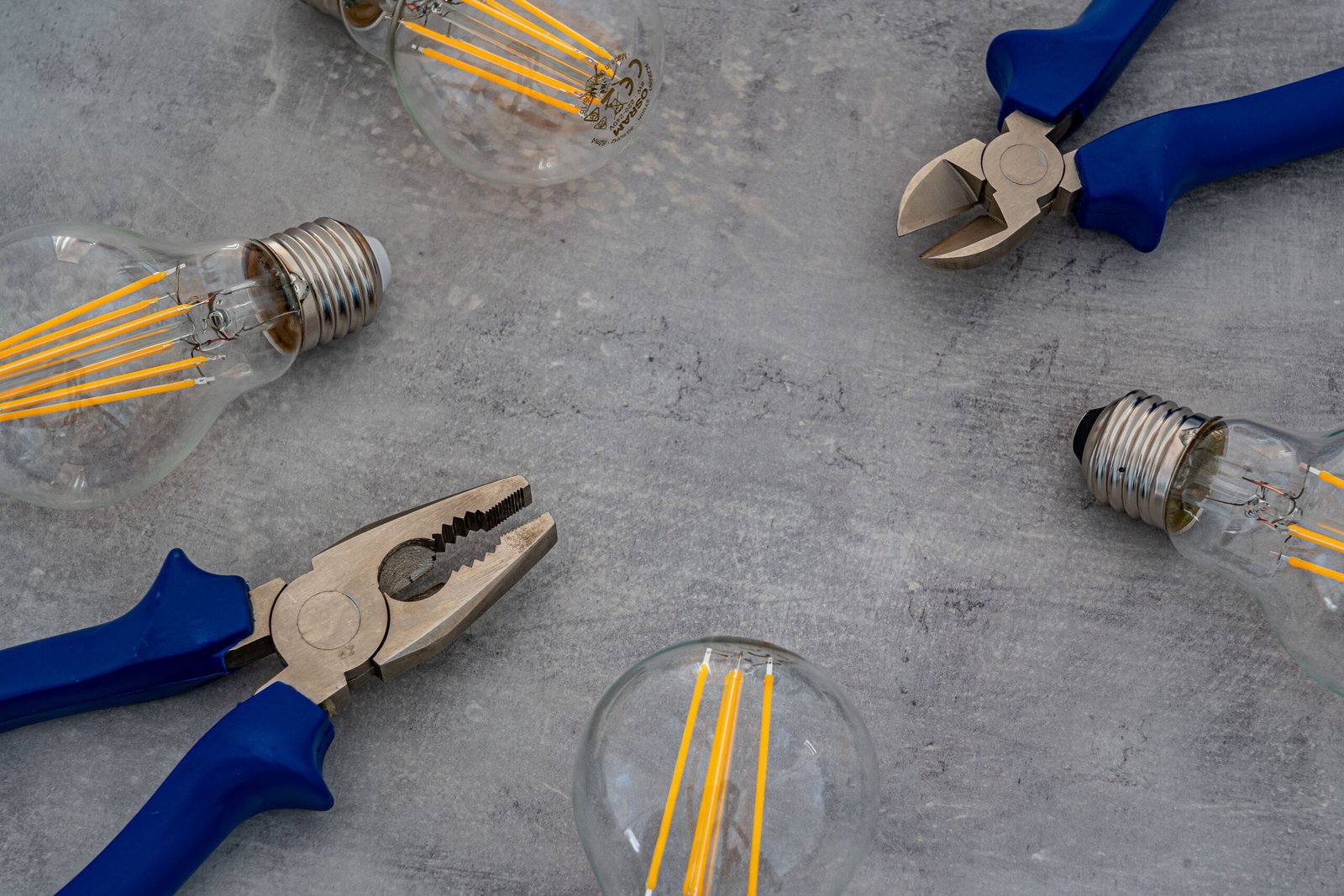 A flat lay of vintage Edison bulbs and pliers on a gray surface, emphasizing industrial design. and electrical repair